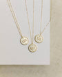 Three gold necklaces with circular pendants displaying numbers on a neutral background
