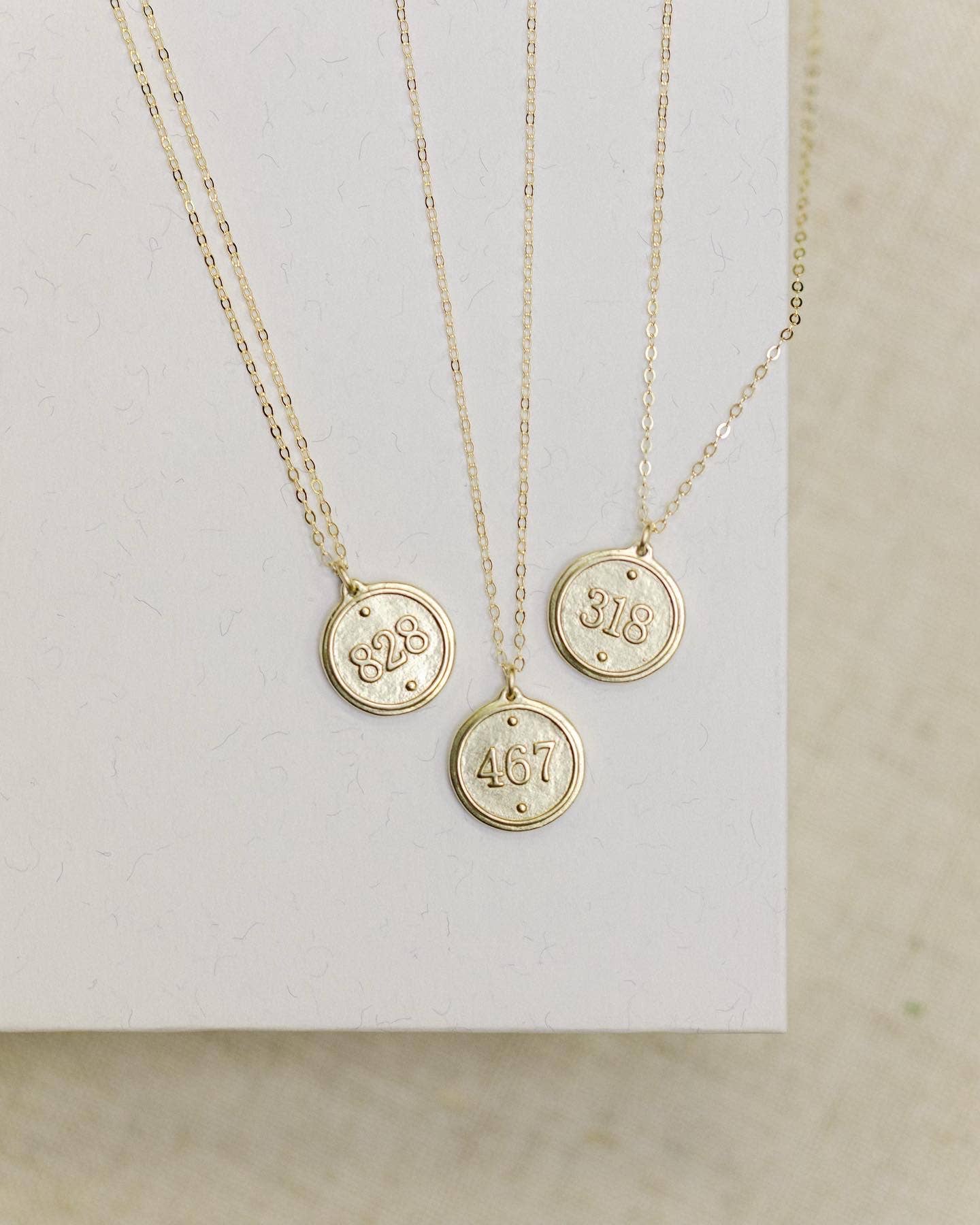 Three gold necklaces with circular pendants displaying numbers on a neutral background