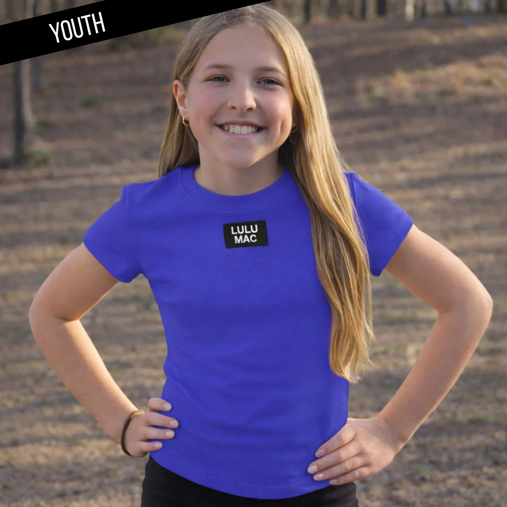 Young girl wearing a blue t-shirt with 'LULU MAC' logo outdoors.