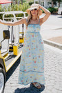 Woman in a long, light blue dress with a pattern of boats and people, standing on a street.