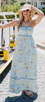 Woman in a long, light blue dress with a pattern of boats and people, standing on a street.