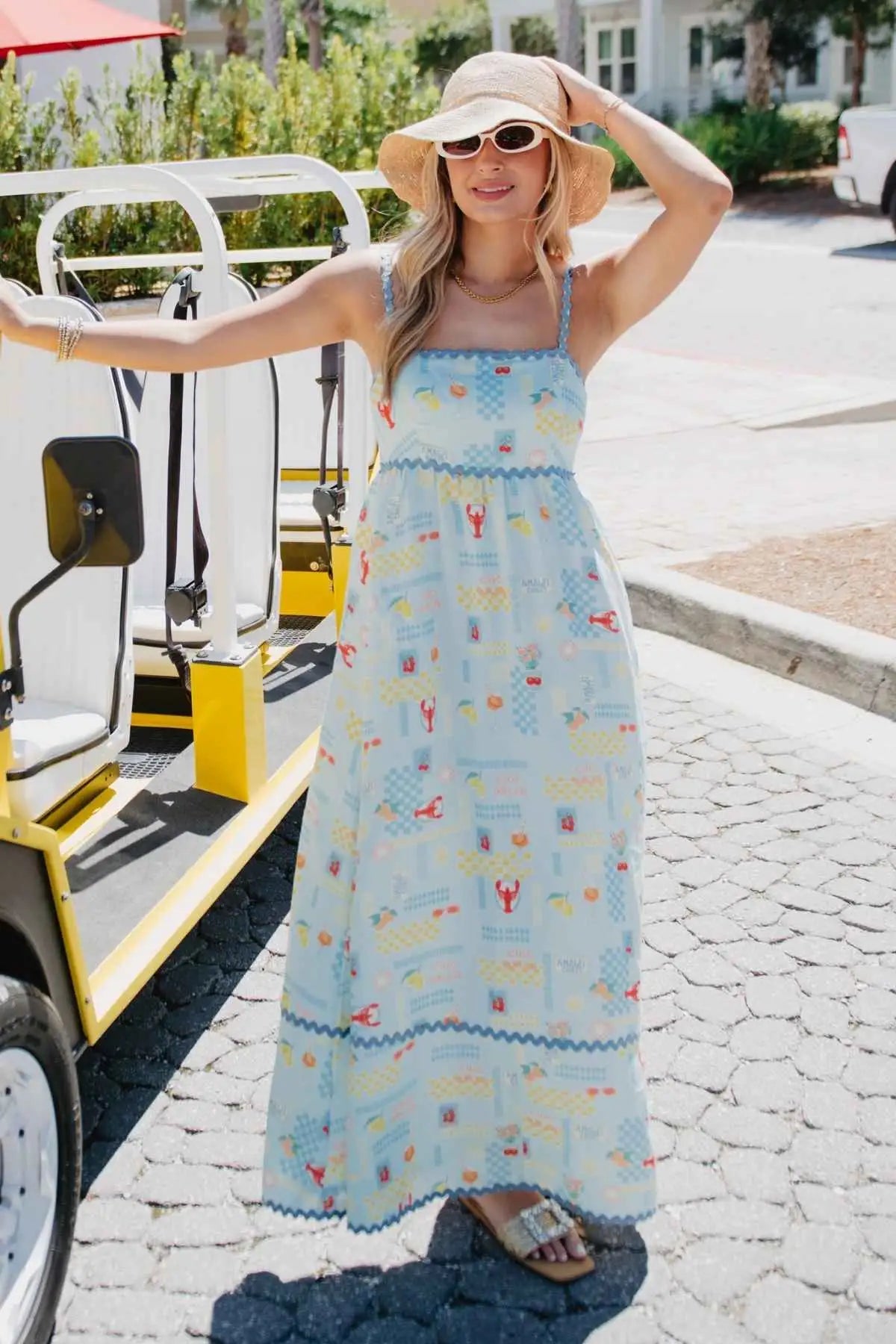 Woman in a long, light blue dress with a pattern of boats and people, standing on a street.