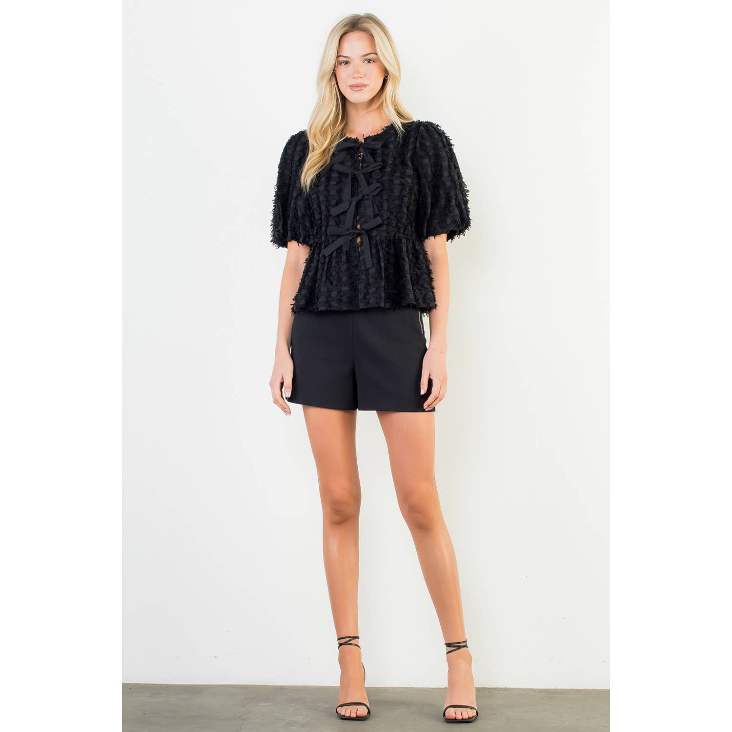 Woman wearing a black textured top and black shorts on a white background