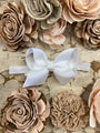 White bow on a headband surrounded by beige and brown floral decorations on a textured surface