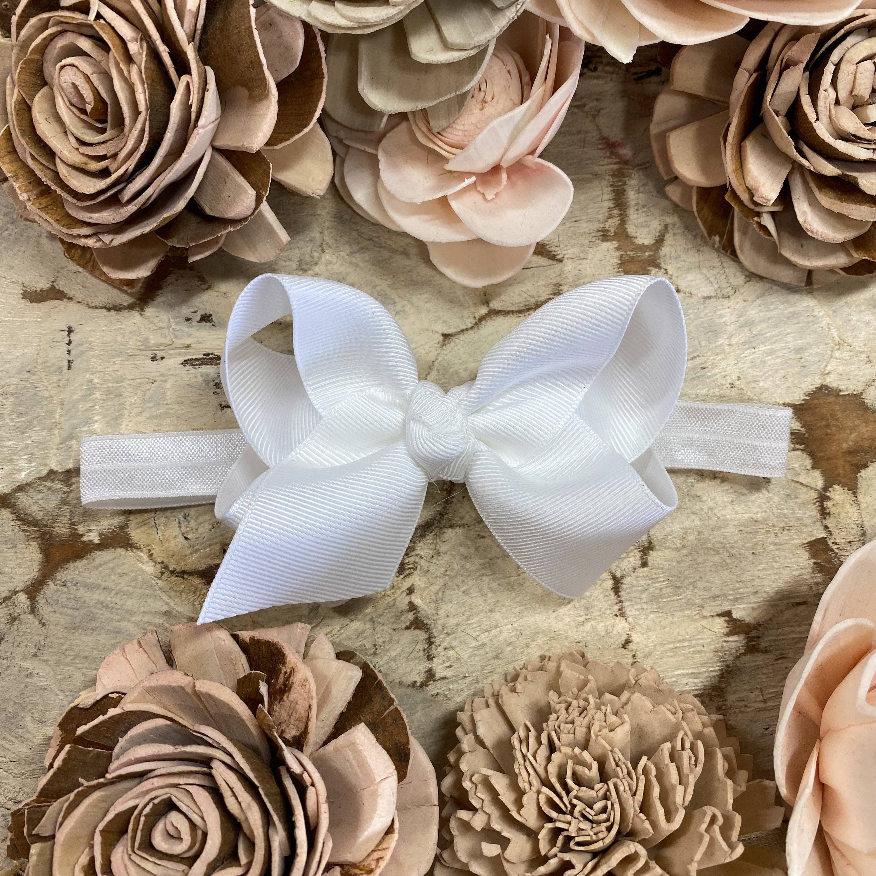 White bow on a headband surrounded by beige and brown floral decorations on a textured surface