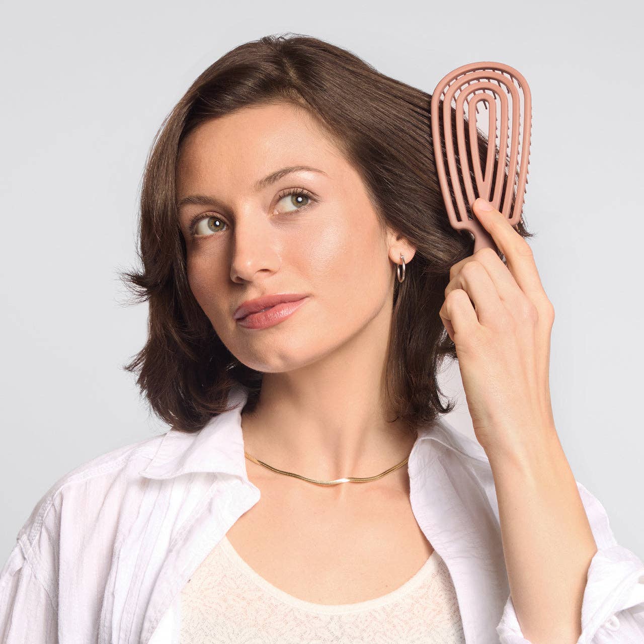 Woman brushing her hair with a rose gold comb against a light gray background