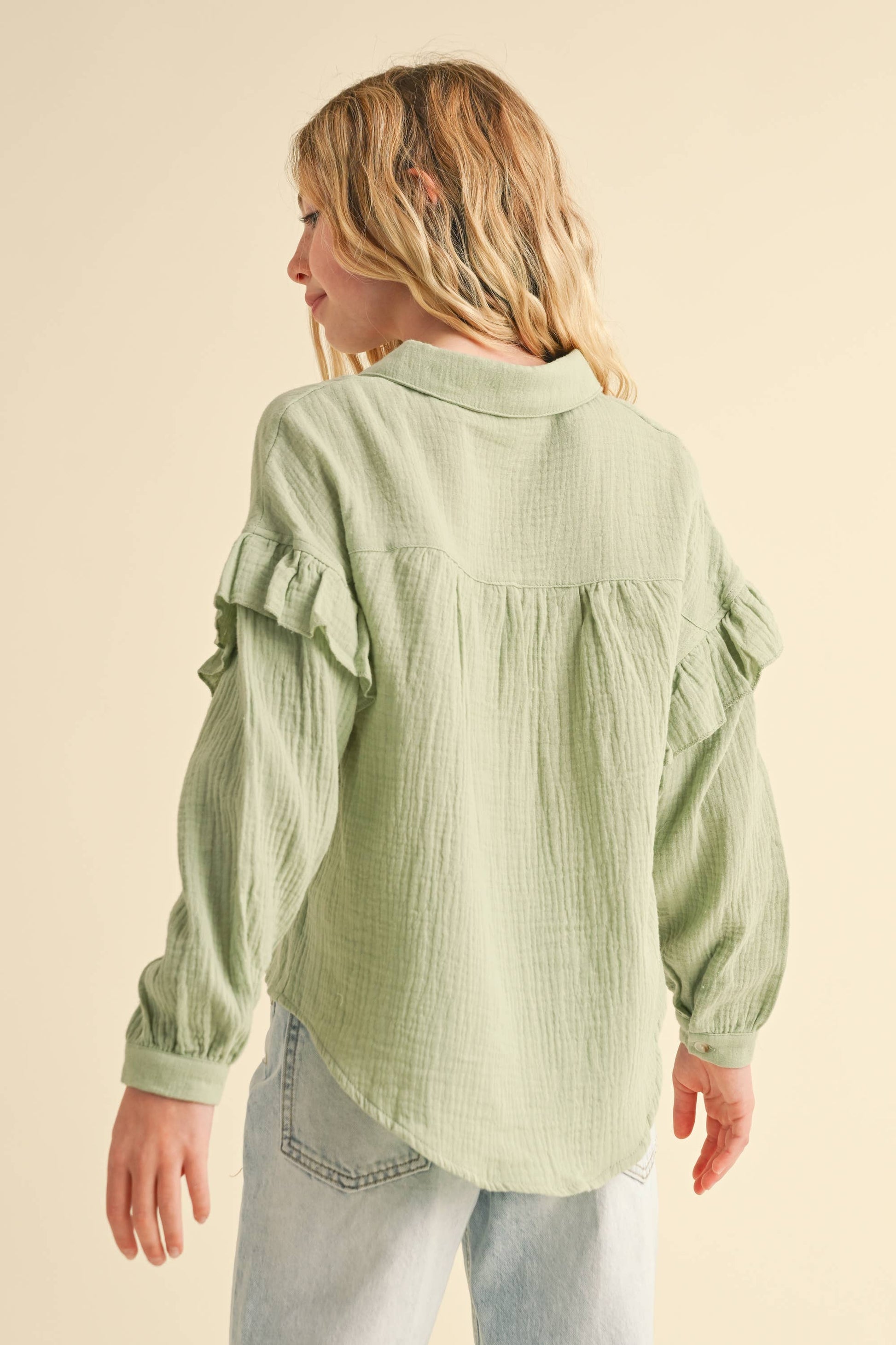 Woman wearing a light green textured blouse with ruffled sleeves on a beige background