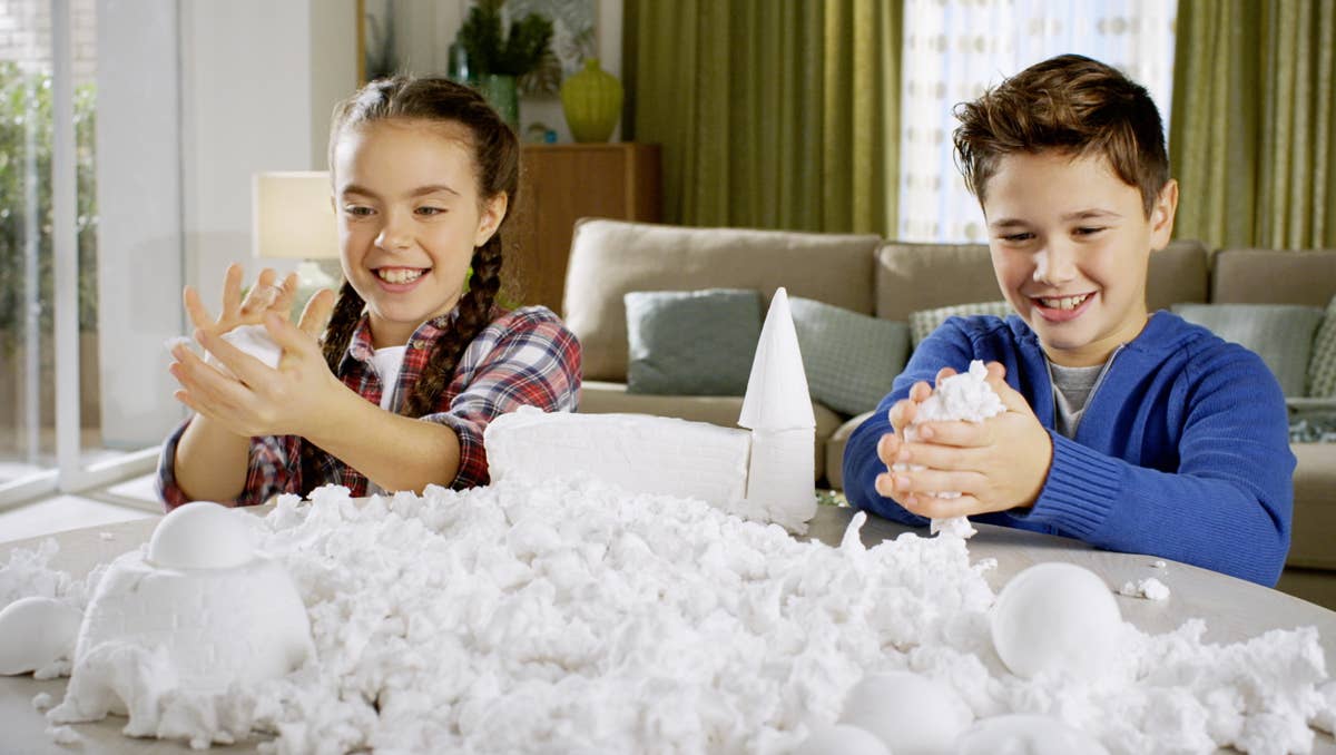 Two children playing with white cotton balls in a living room.