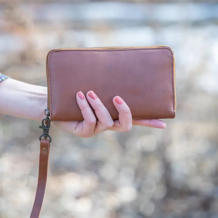 Brown leather wallet held by a hand with a blurred natural background
