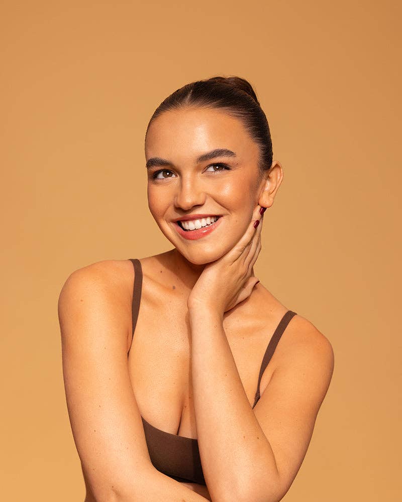 Woman wearing a brown strappy top against a beige background