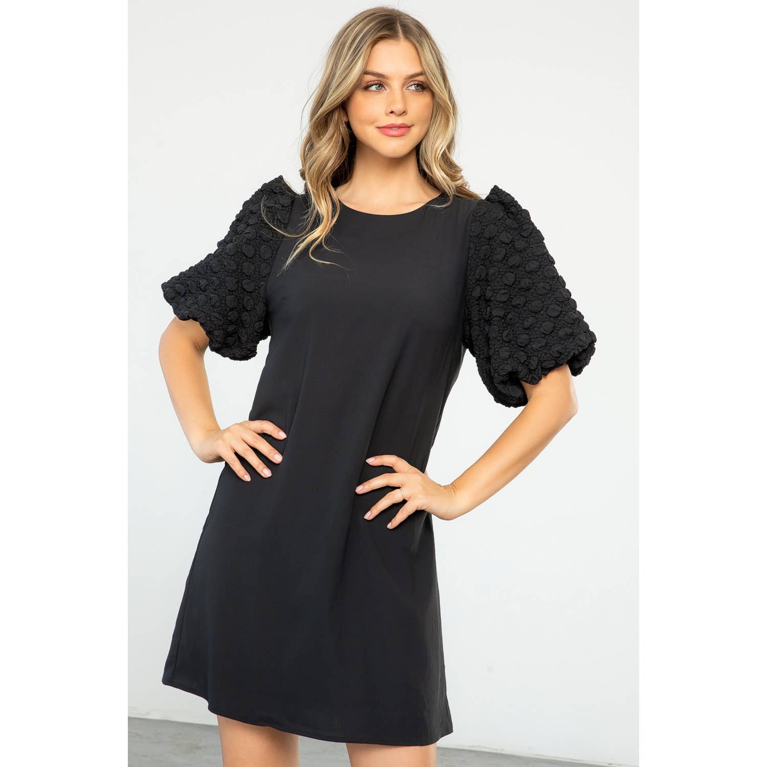 Woman wearing a black dress with ruffled sleeves against a white background