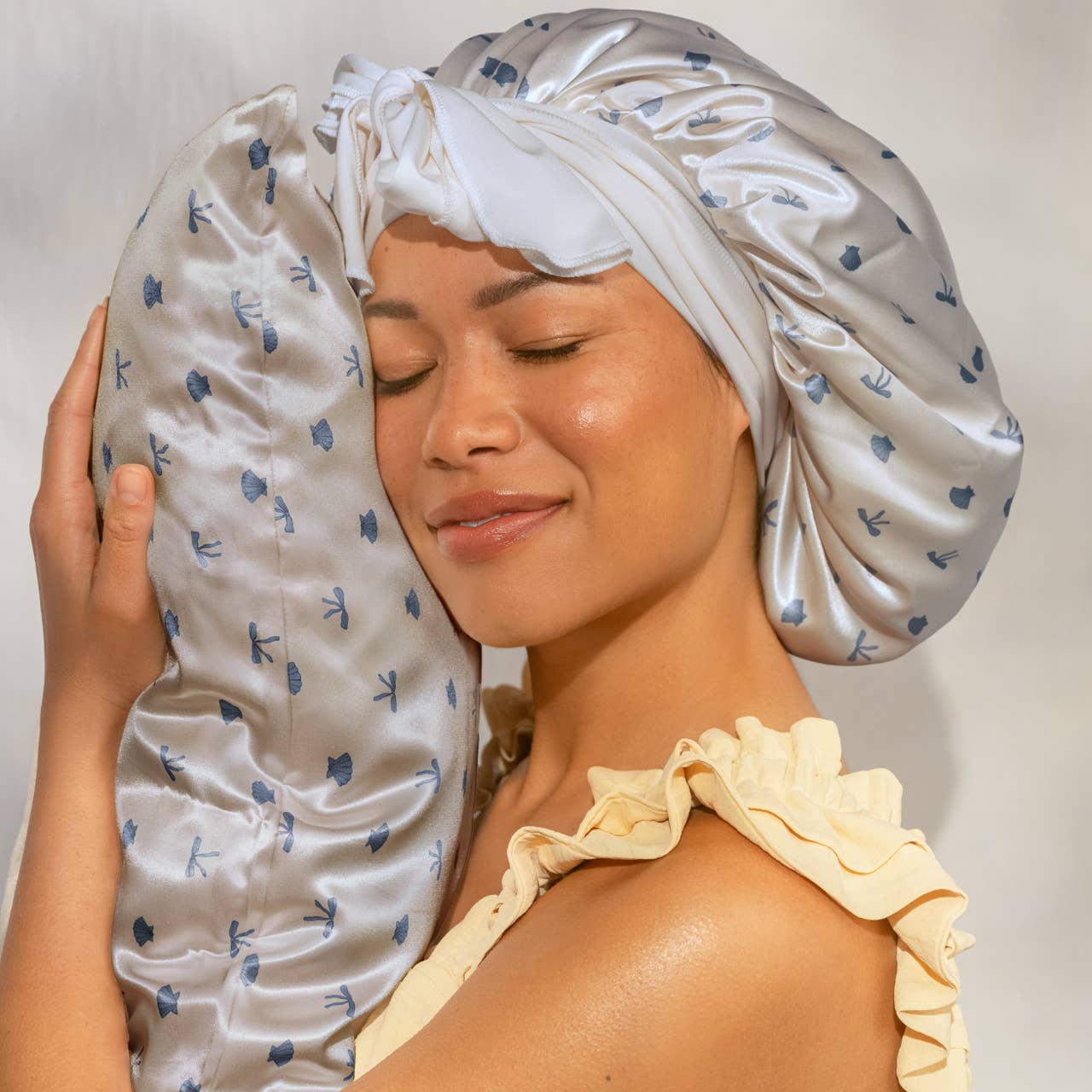 Woman wearing a satin headband and holding a matching pillow with a white background