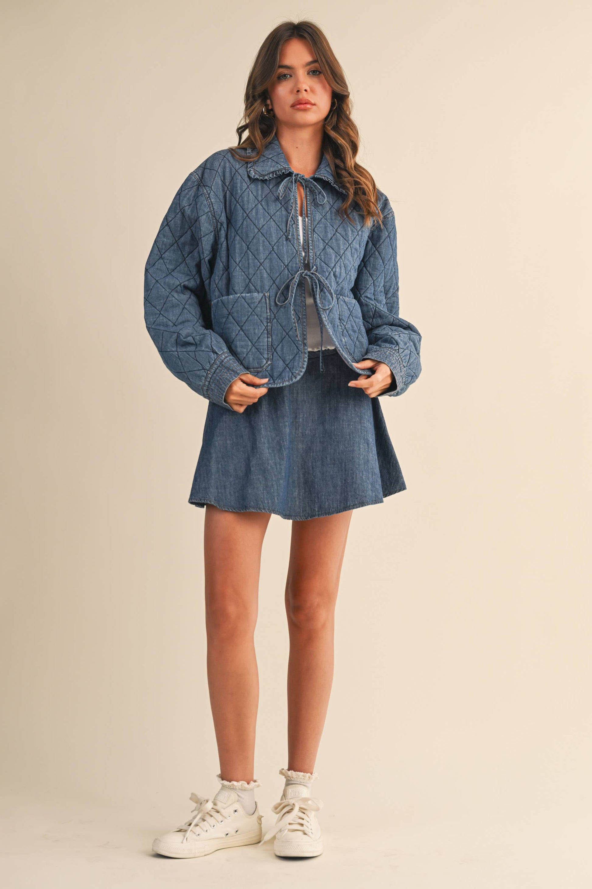 Woman wearing a blue quilted jacket with a skirt against a beige background