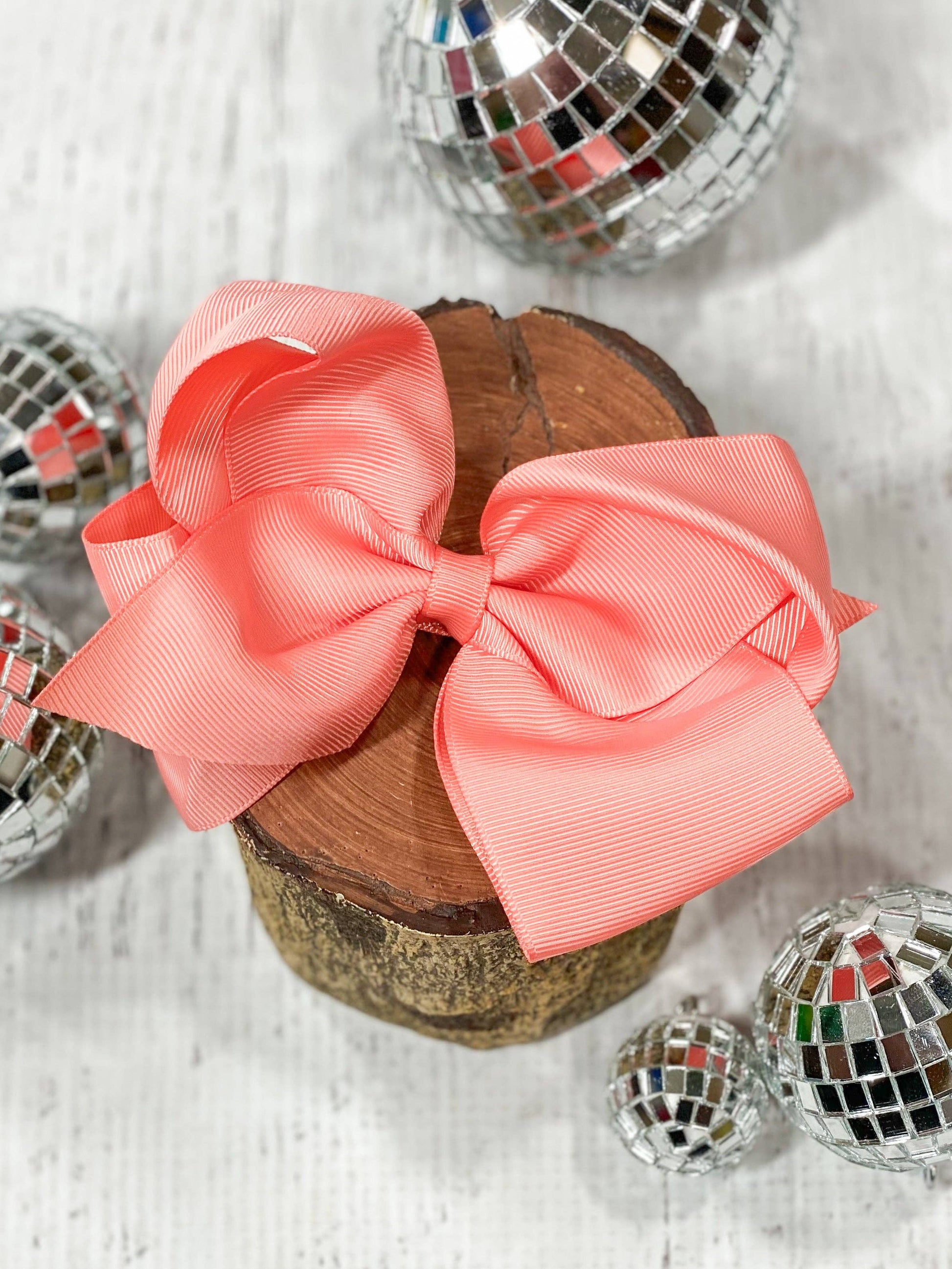 Two coral bows on a wooden block with disco balls in the background