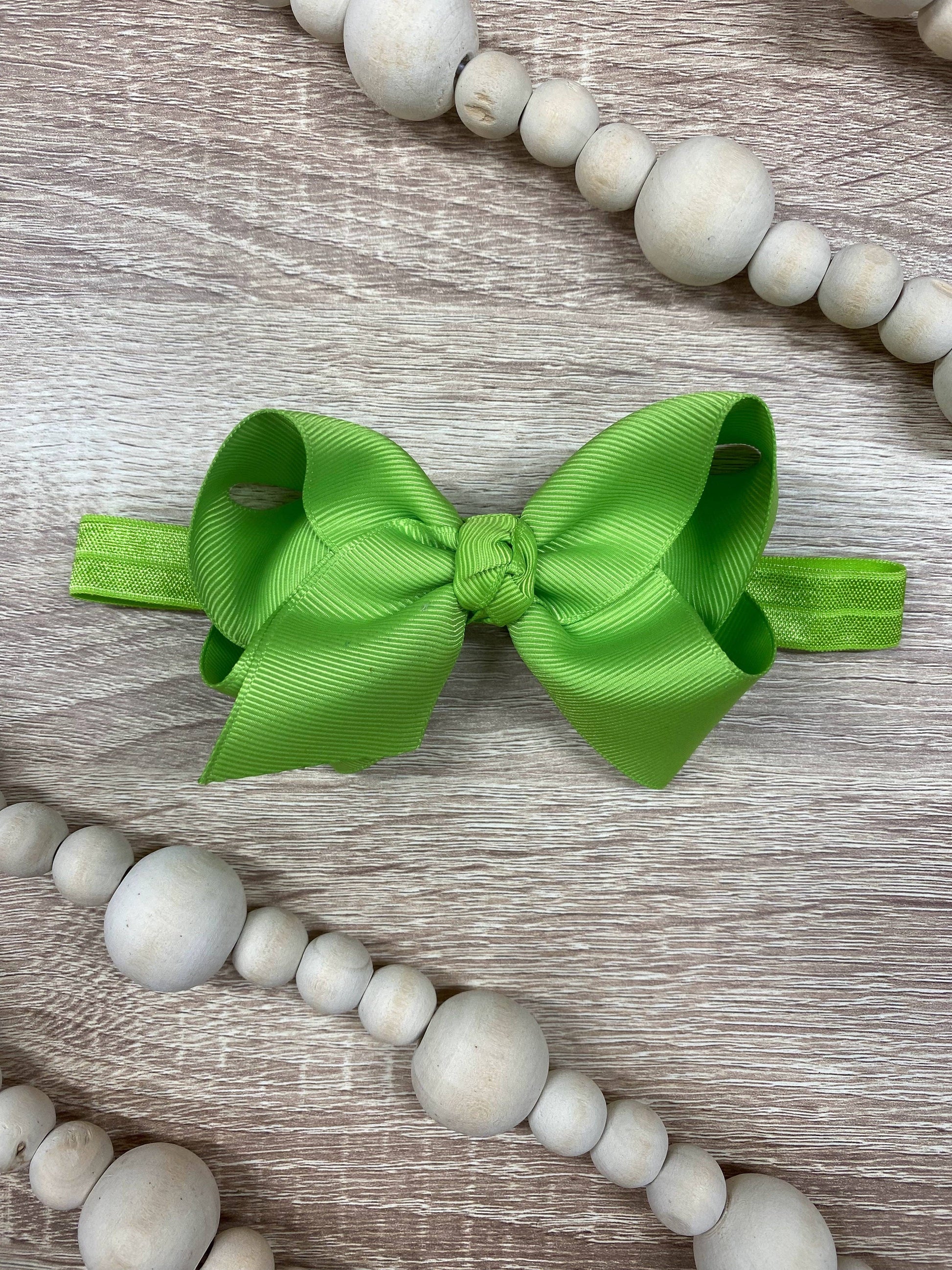 Green bow hair accessory on a wooden surface with wooden beads