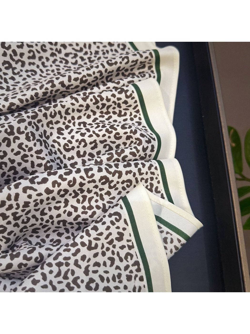 Leopard print bandana close-up with green-trimmed cream border and folded triangles