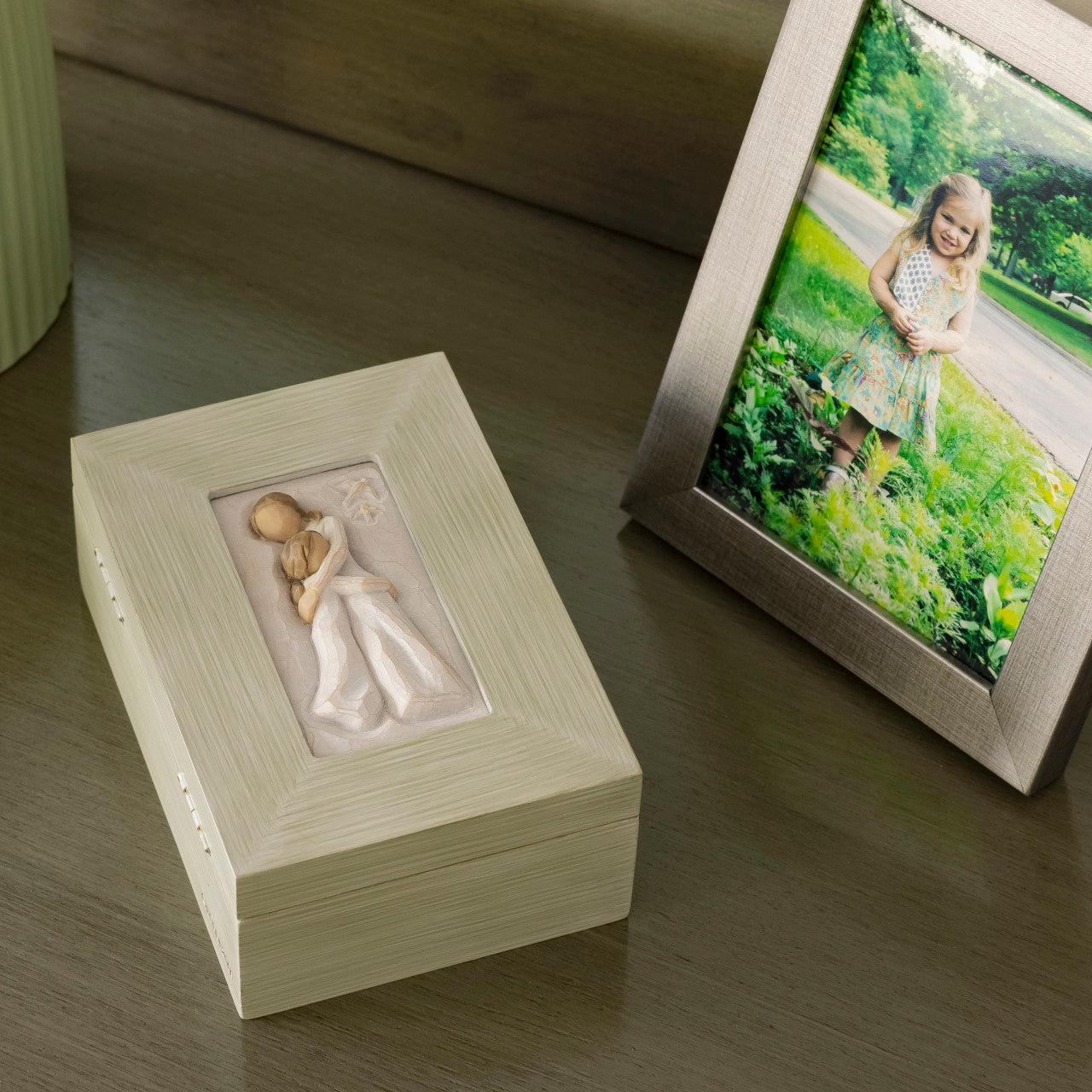 Wooden box with a figurine of a child holding her mother, next to a framed photo of two children outdoors.