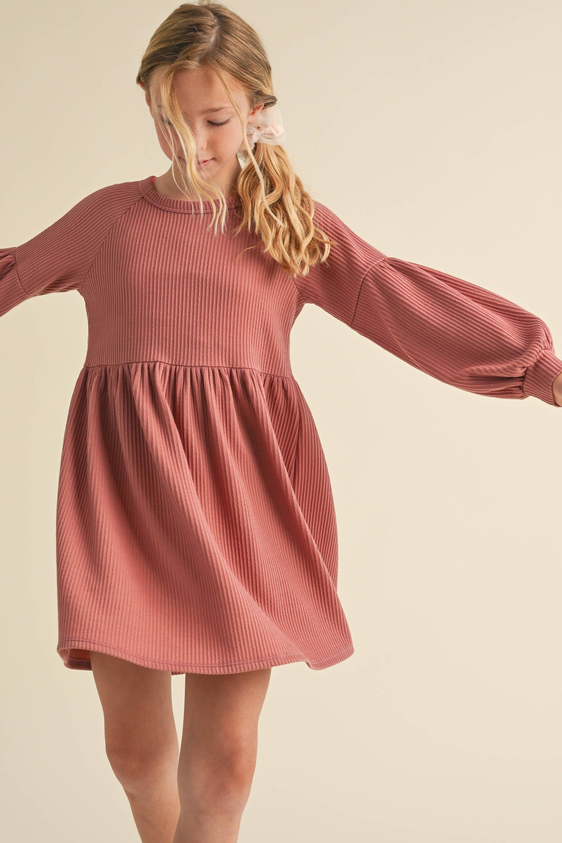 Young girl wearing a pink ribbed dress against a beige background