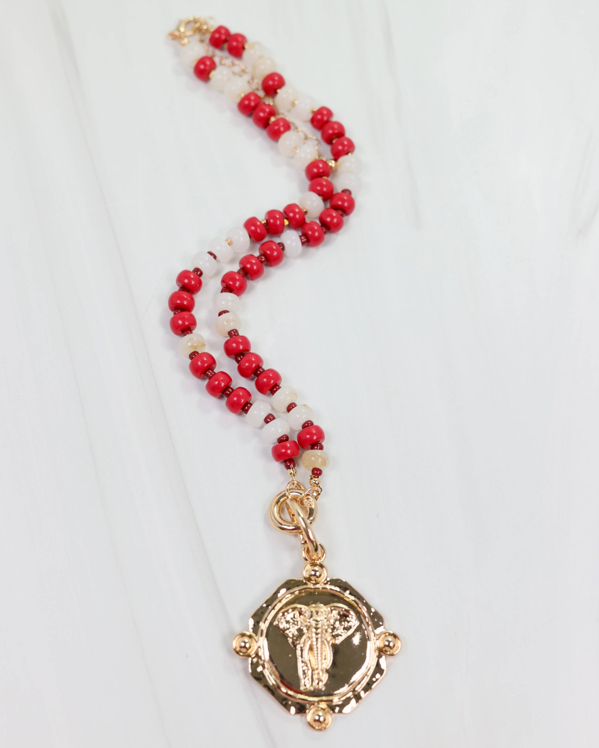 Necklace with red and white beads and a gold pendant on a white background