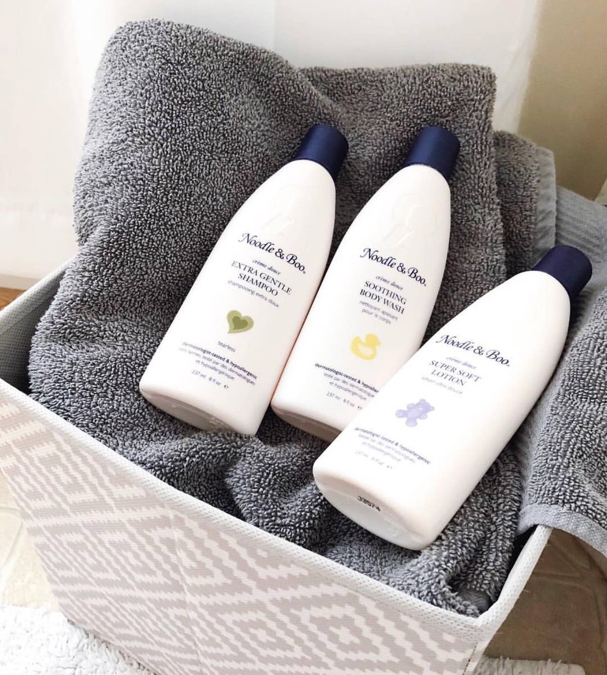 Three bottles of Noodle & Boo products on a gray towel inside a white basket.