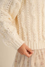 Close-up of a person wearing a cream-colored knitted sweater with a textured pattern.