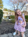 Two young girls in matching floral dresses standing outdoors with a blurred background.