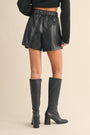 Person wearing black leather shorts and knee-high boots on a beige background
