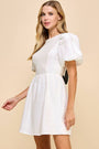 Woman wearing a white dress with puff sleeves against a beige background