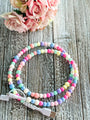 Colorful beaded phone charger on a wooden surface with flowers in the background
