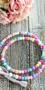 Colorful beaded phone charger on a wooden surface with flowers in the background