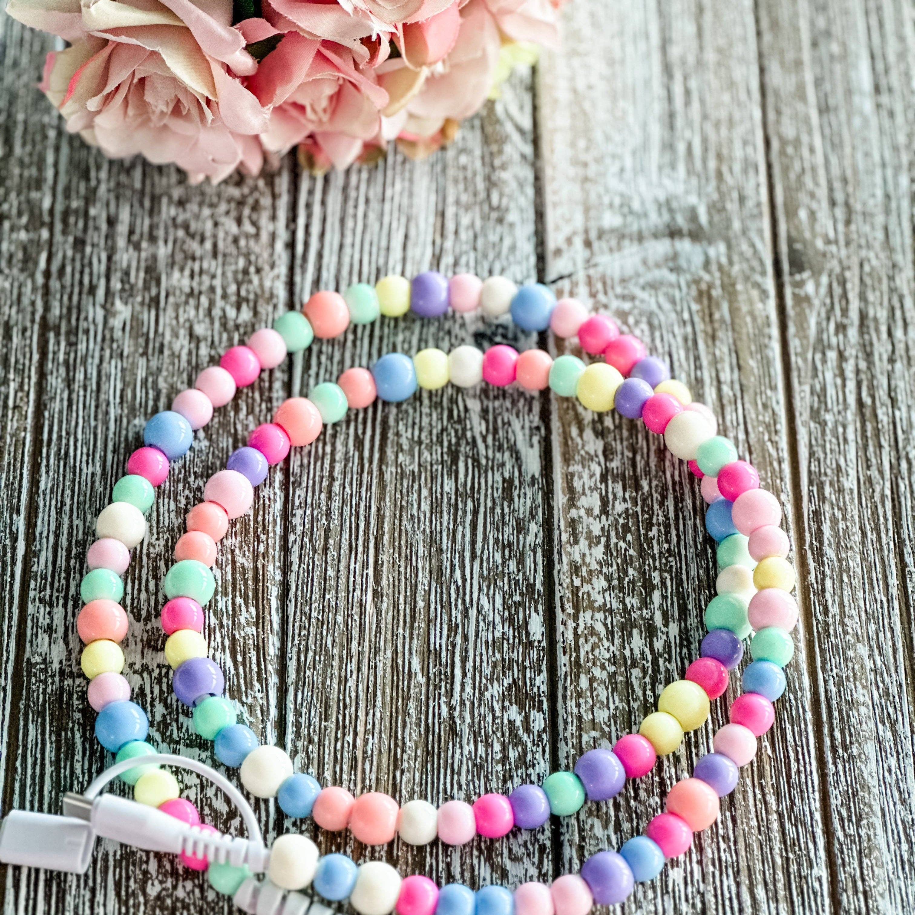Colorful beaded phone charger on a wooden surface with flowers in the background