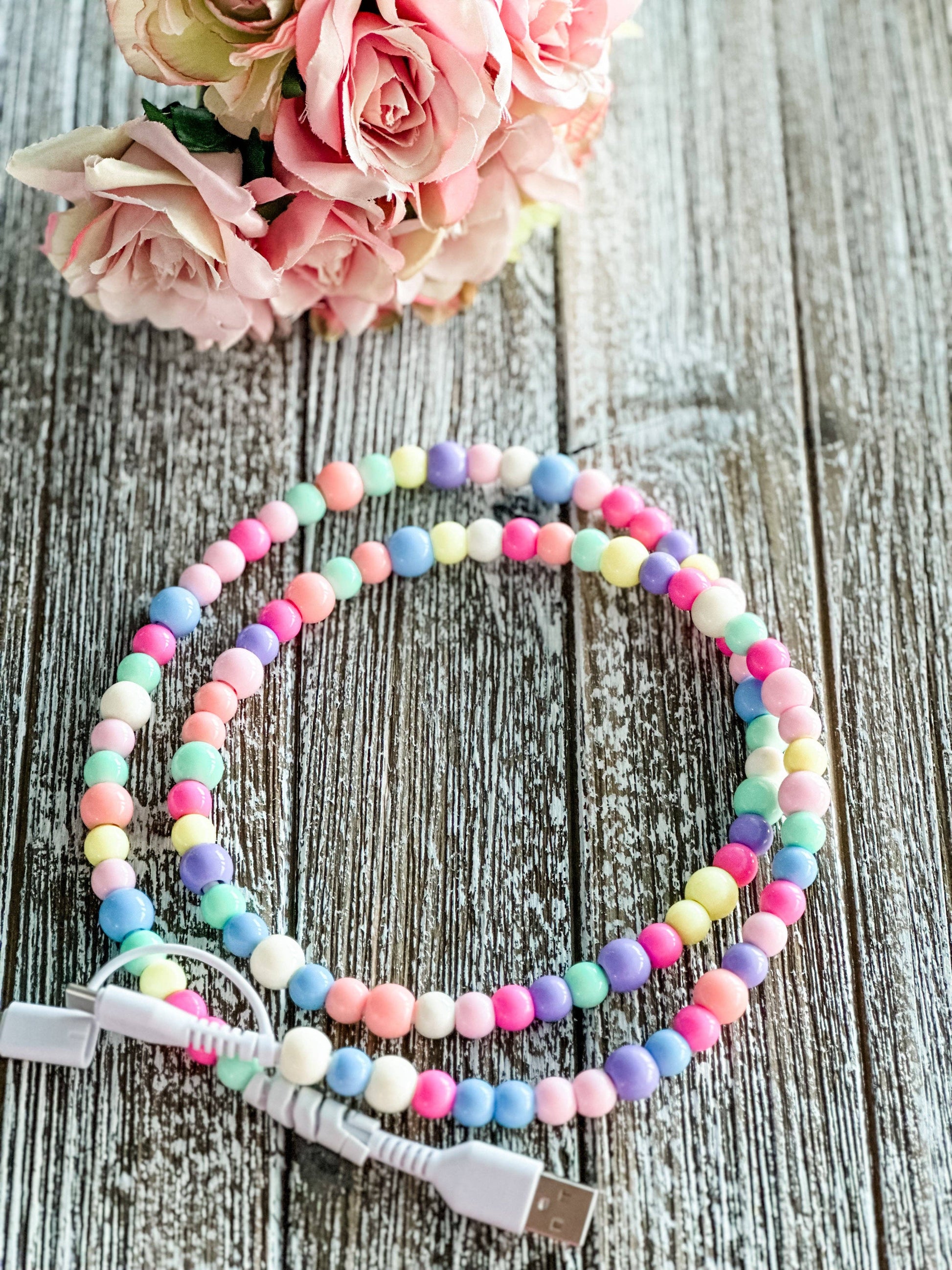 Colorful beaded phone charger on a wooden surface with flowers in the background