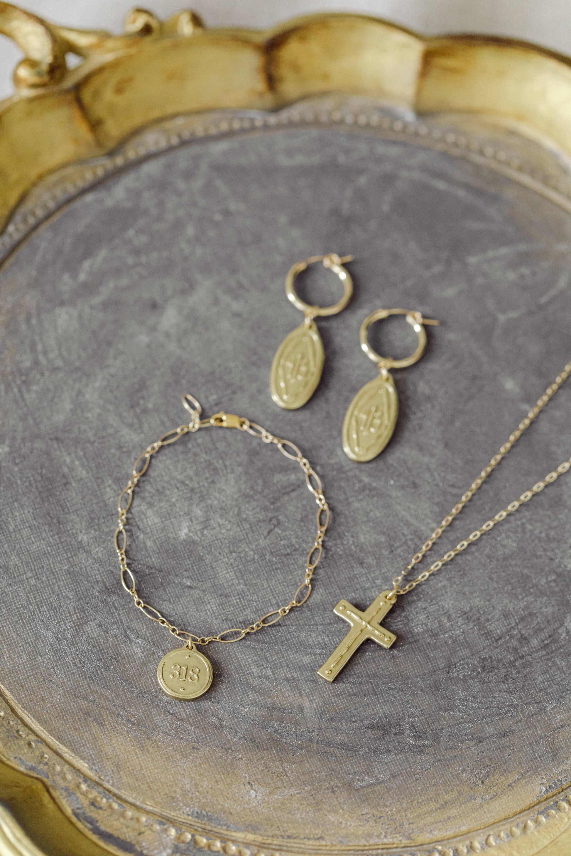 Gold jewelry set including bracelet, necklace, and earrings on a gray surface with a gold frame.
