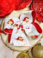 Decorative bow with Santa Claus design on a wooden surface with Christmas ornaments.