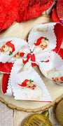 Decorative bow with Santa Claus design on a wooden surface with Christmas ornaments.
