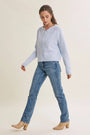 A woman modeling a light blue knit cardigan sweater, blue jeans, and beige ankle boots against a plain cream studio background.