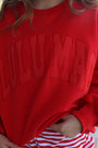 Red sweatshirt with 'ILLUMATI' text worn by a person, outdoor setting