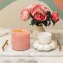 Pink candle, white mug, and vase with pink flowers on a marble surface