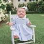 Baby in a high chair wearing a light blue outfit with a pattern, outdoors.