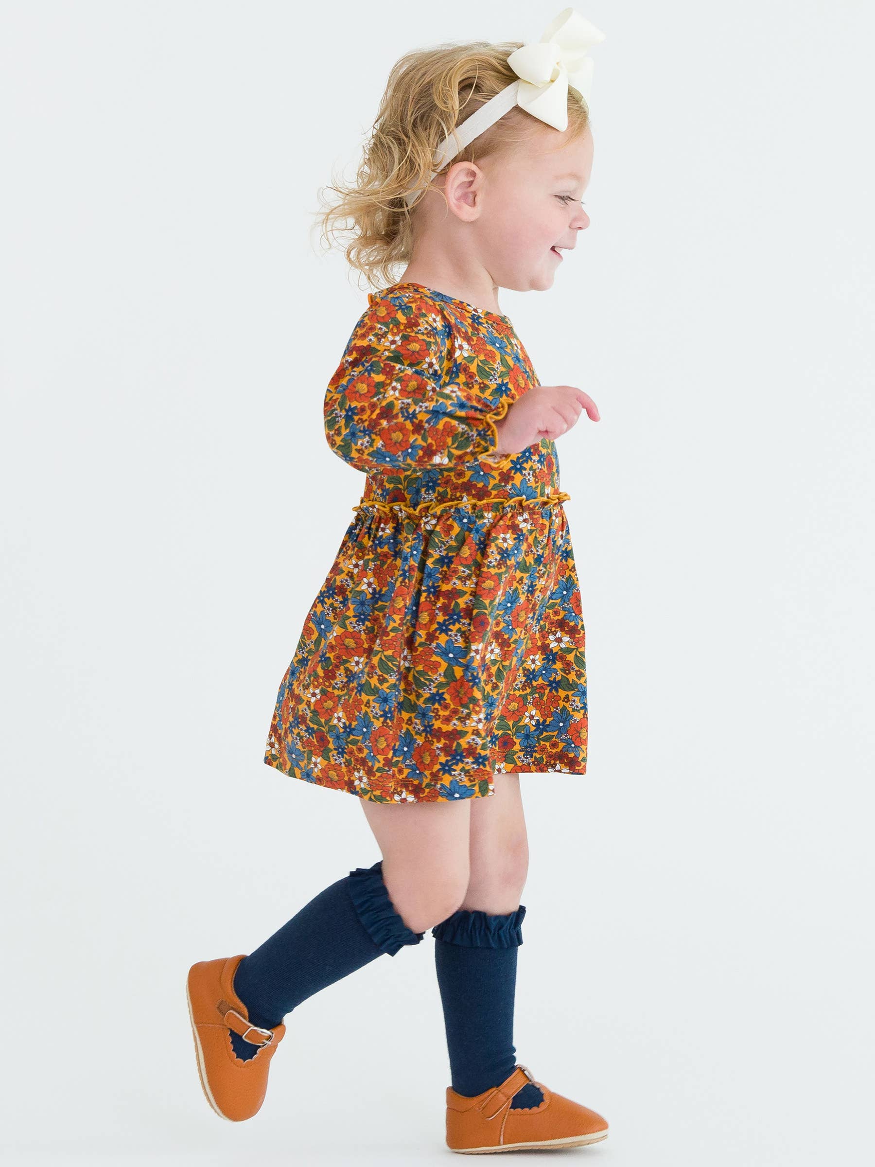 Child wearing a colorful floral dress with navy socks and orange shoes on a white background