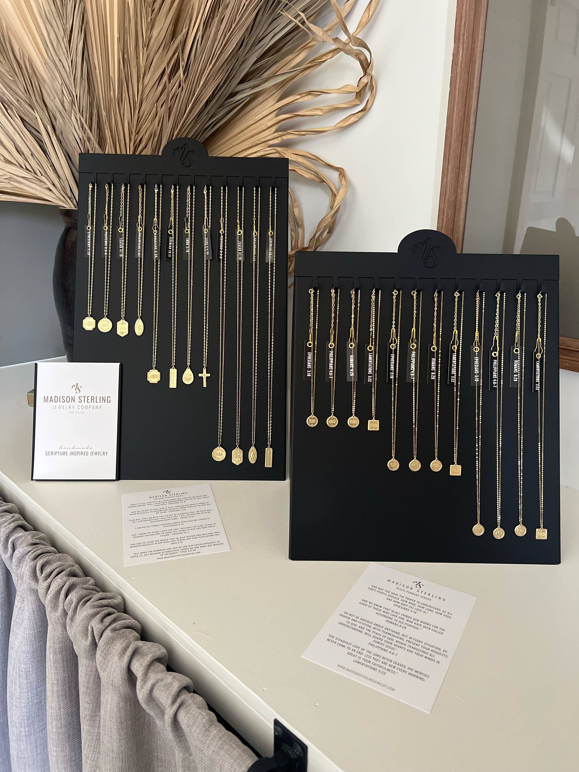 Two black display cards with necklaces on a white surface with a decorative background.