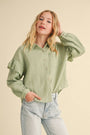 Woman wearing a green textured shirt and light blue jeans against a beige background