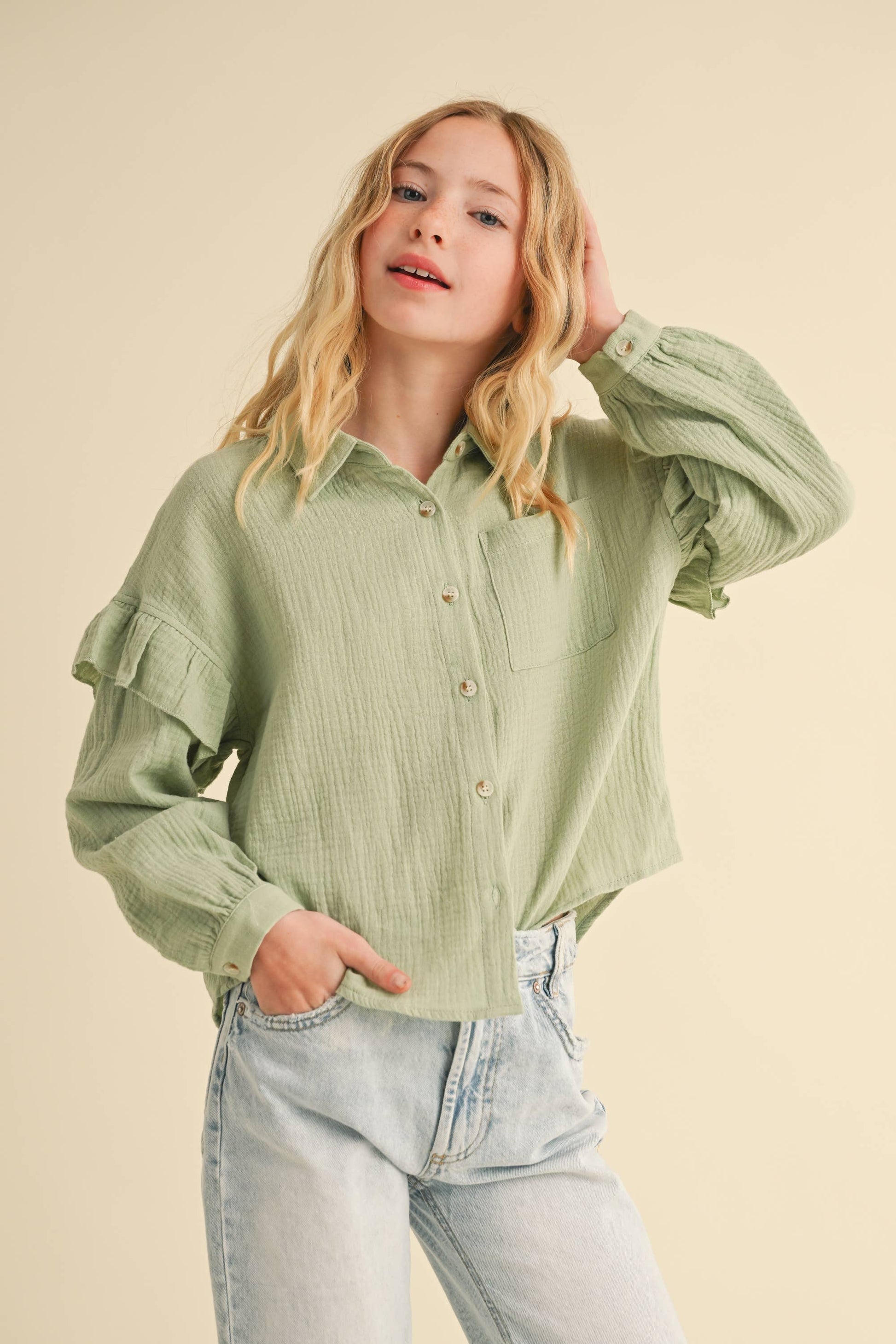 Woman wearing a green textured shirt and light blue jeans against a beige background