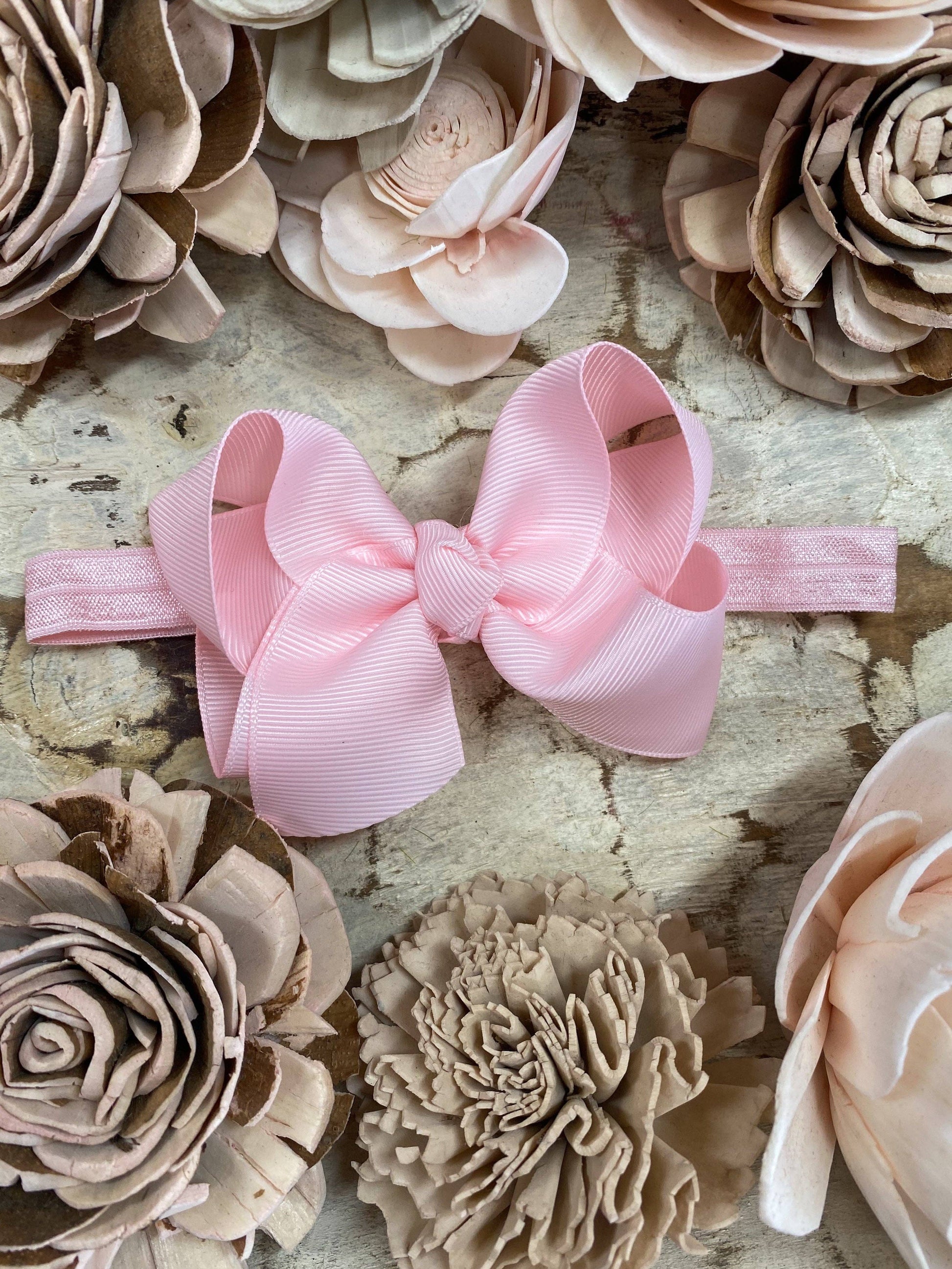 Pink hair bow on a headband surrounded by beige and brown flowers