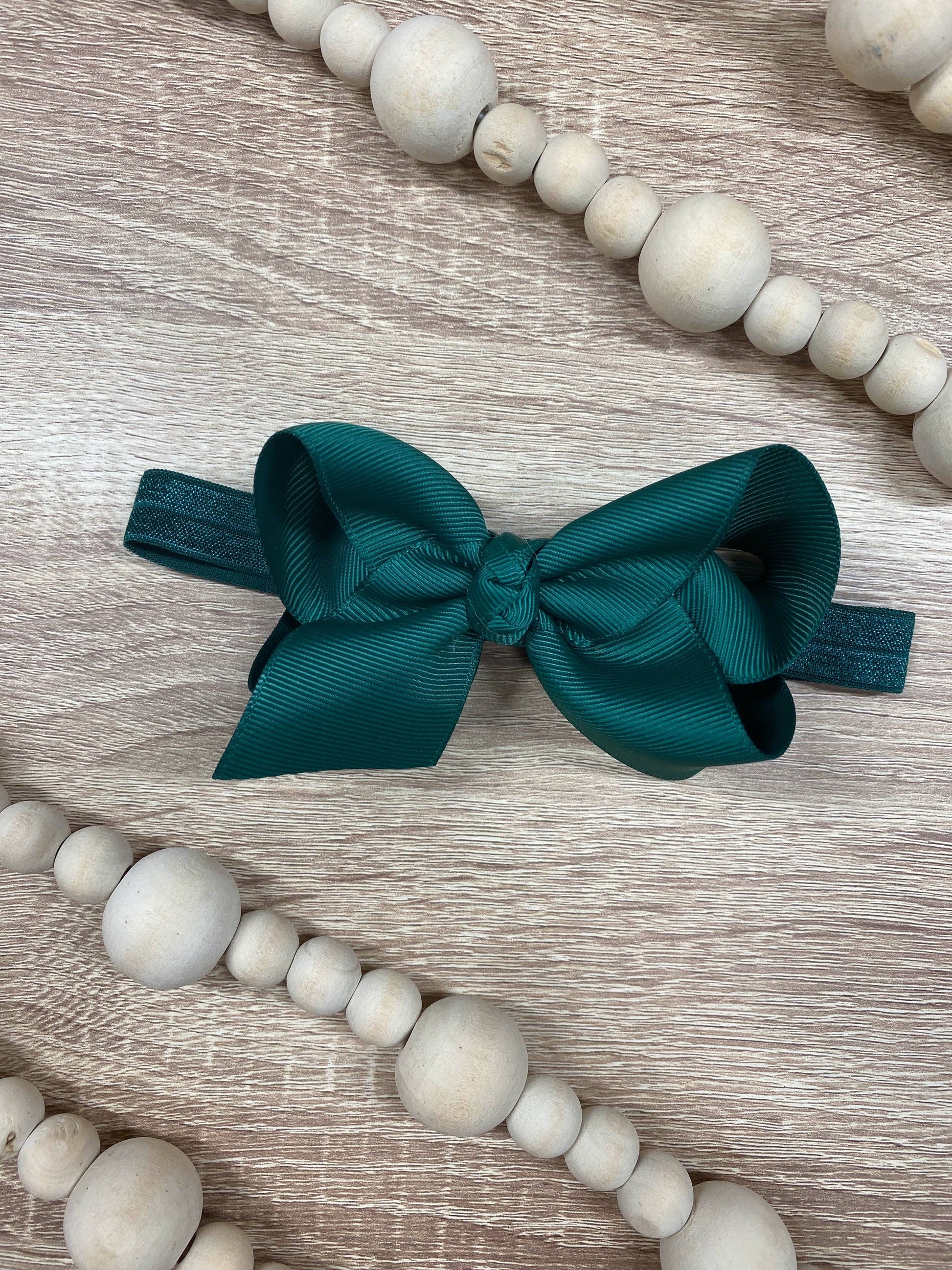 Teal bow on a wooden surface with white beads