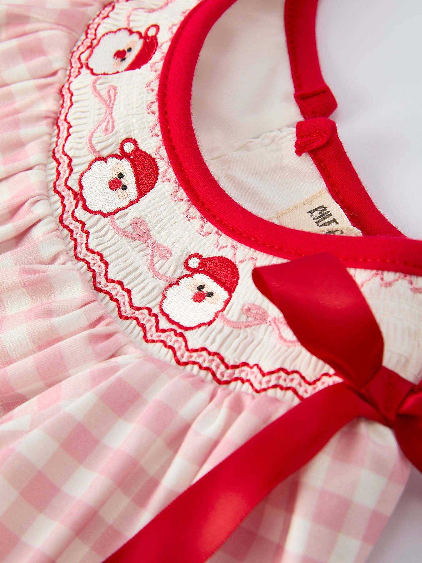 Close-up of a pink checkered dress with red collar and bow, featuring embroidered designs.
