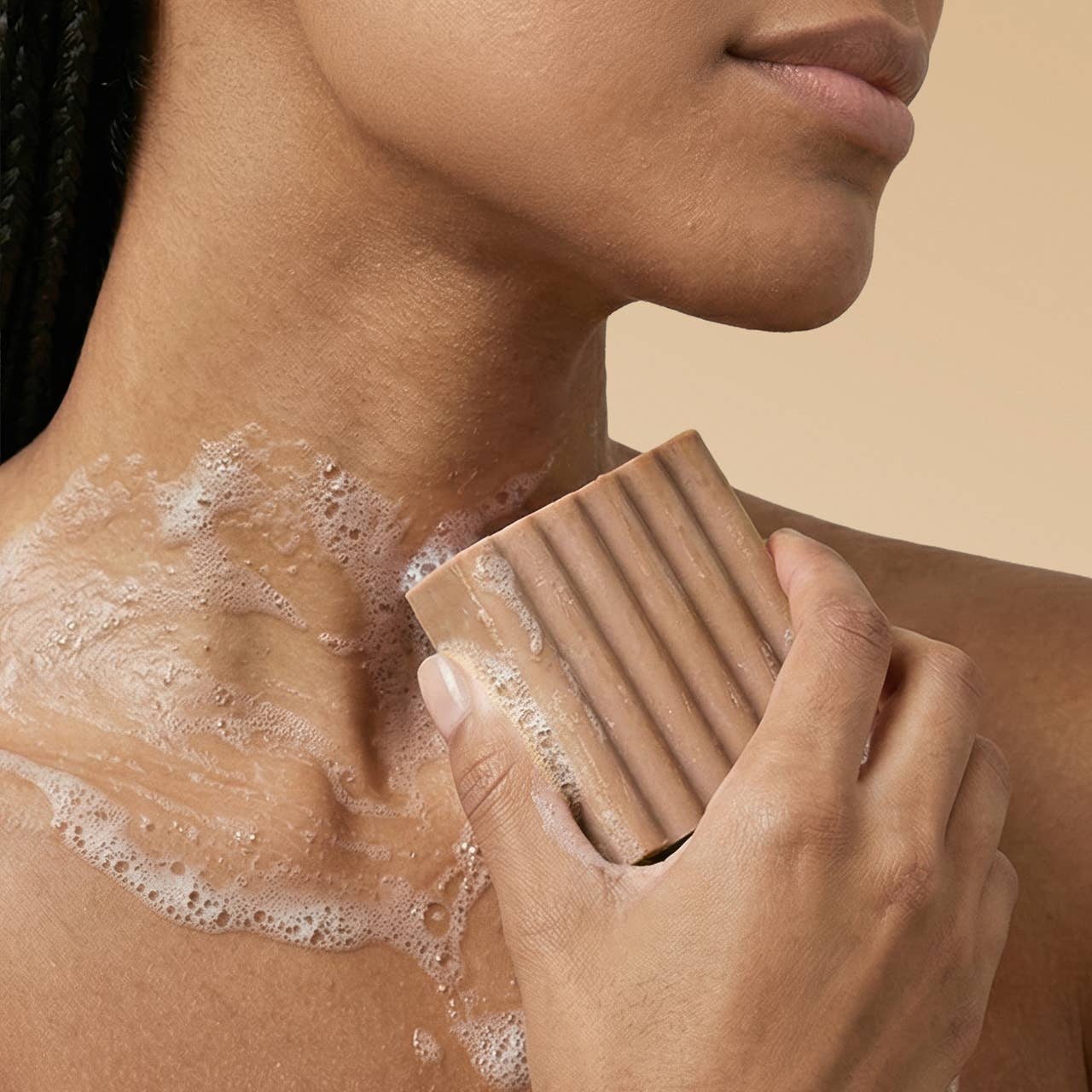 Person using a bar of soap on their shoulder against a beige background