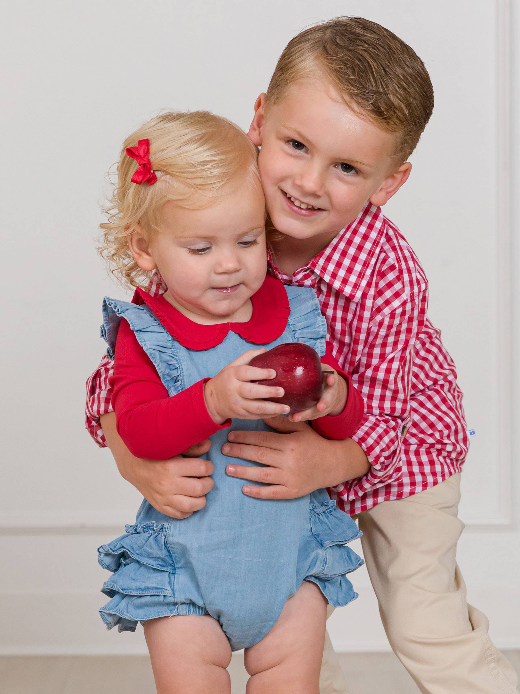 Two children, a boy and a girl, standing close together with a white background.