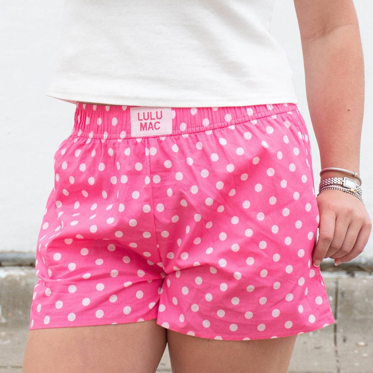 Pink polka dot shorts with 'Lulu Mac' branding worn by a person.
