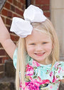 Young girl with a large white bow in her hair, wearing a floral dress.